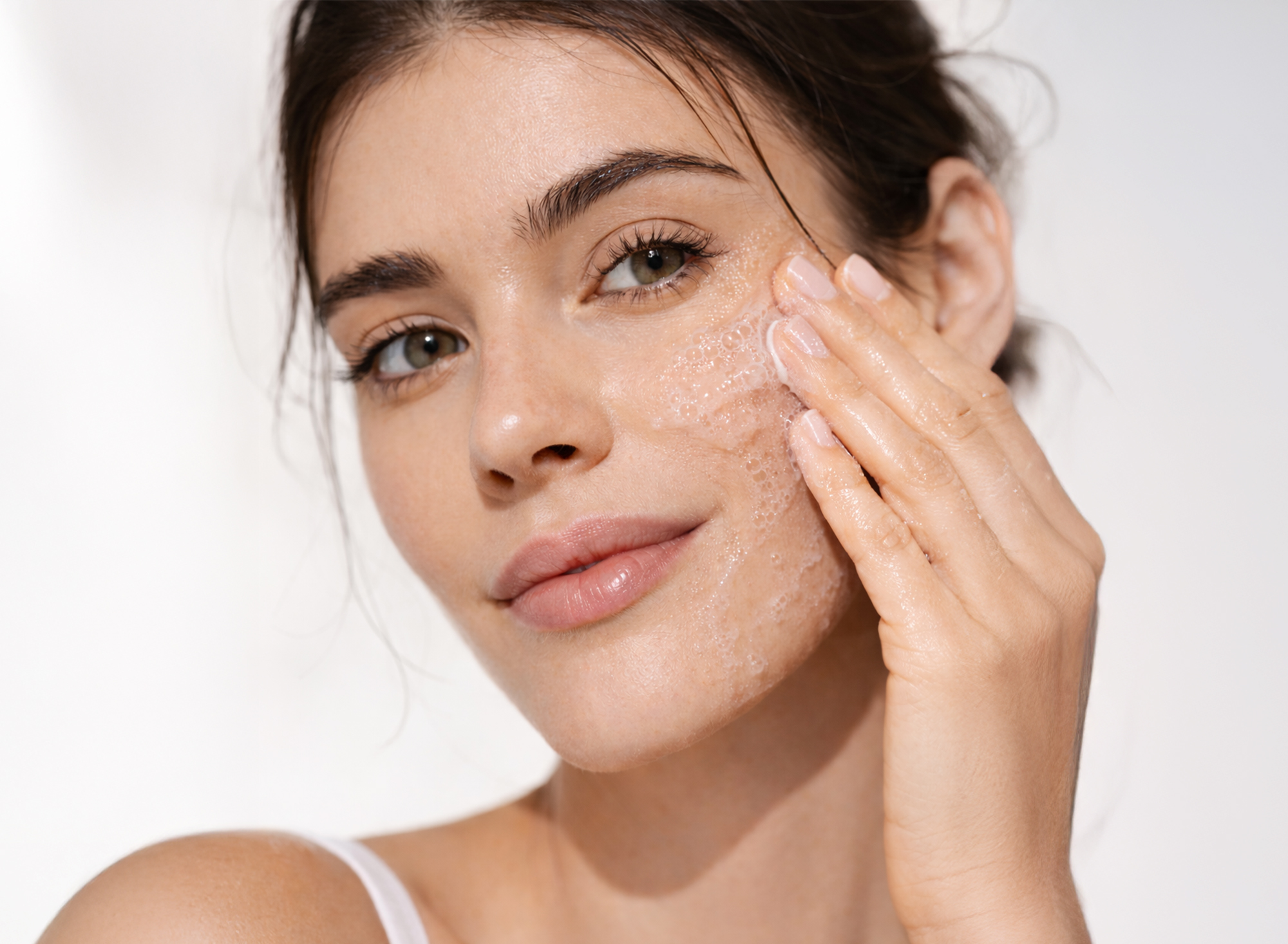 Frau mit braunen Haaren reinigt ihr Gesicht mit einem JEAN D'ARCEL Reinigungs-Schaum und lächelt zur Seite.